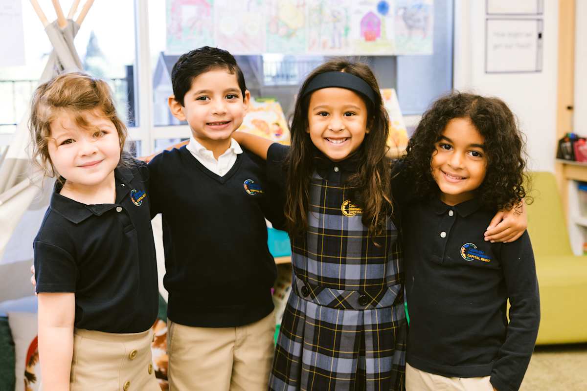 Four elementary students standing in a line with hands on each other's shoulders, all smiling and looking forward together, demonstrating friendship and teamwork at CIS