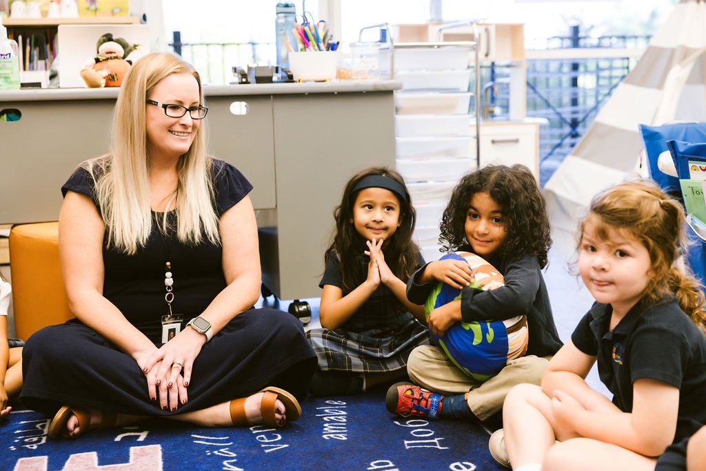 A teacher sitting with students, leading a classroom activity.